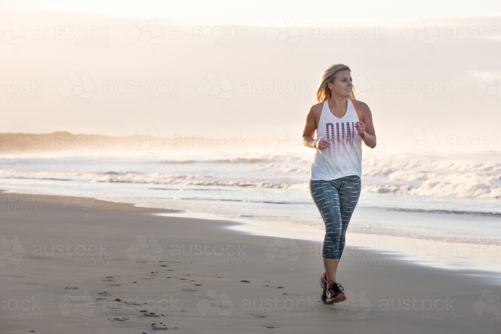woman running on a beach in the early morning - Australian Stock Image