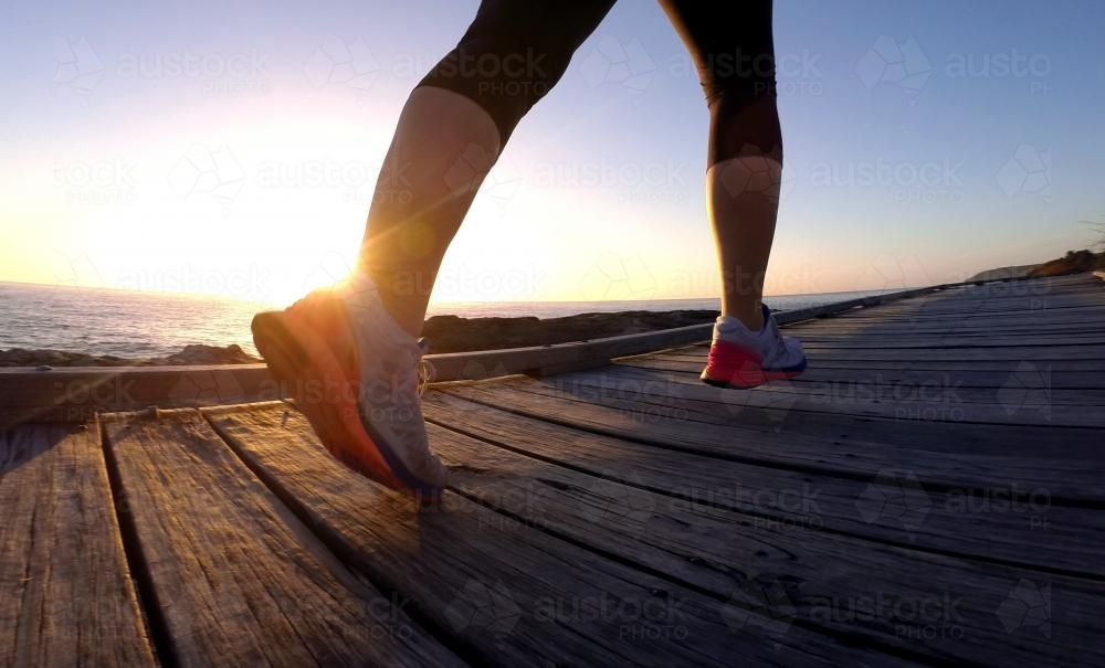 Woman running on boardwalk with lens flare sunrise - Australian Stock Image