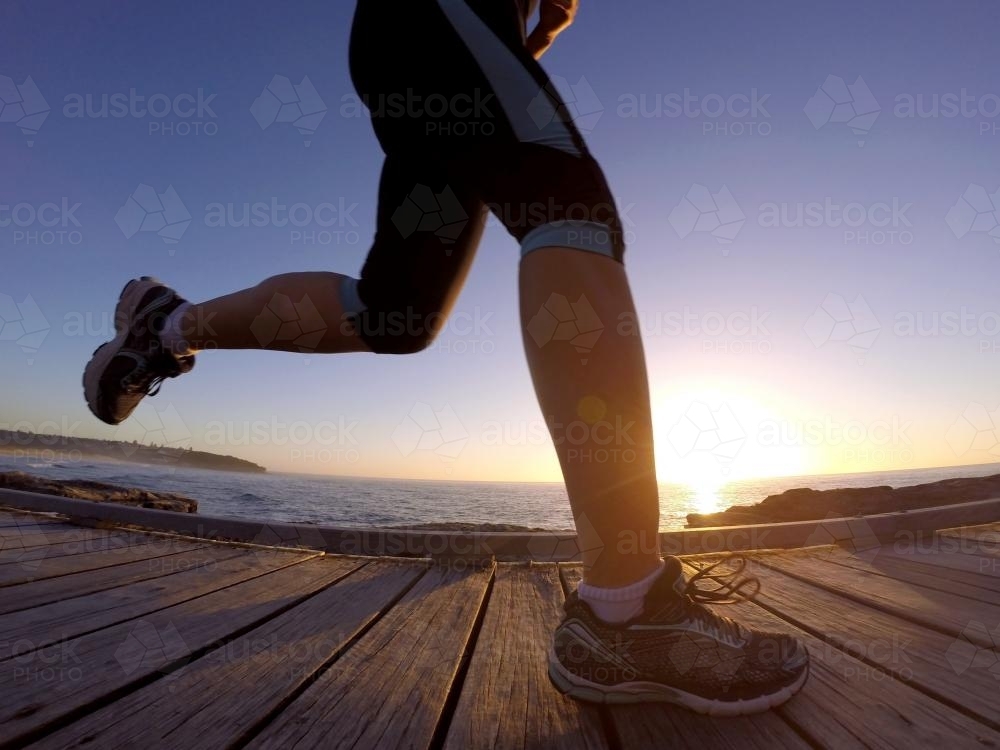 Woman running on coastal boardwalk at sunrise - Australian Stock Image