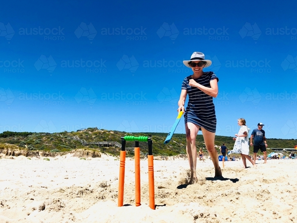 Woman running to cricket wicket on beach playing beach cricket - Australian Stock Image