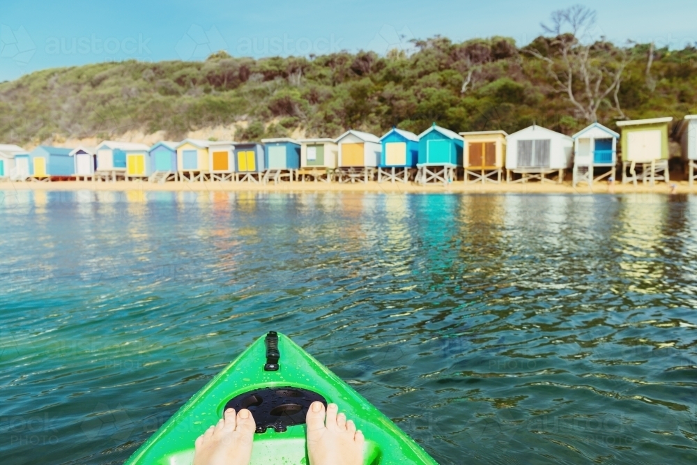 woman's feet in kayak in the ocean with colorful beach huts on the shore - Australian Stock Image