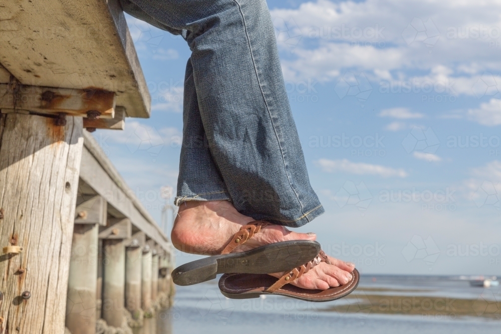 Woman's feet in sandals off the edge of a timber pier - Australian Stock Image