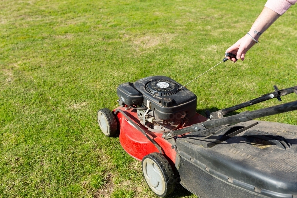 woman's hand pulling start rope on lawnmower - Australian Stock Image