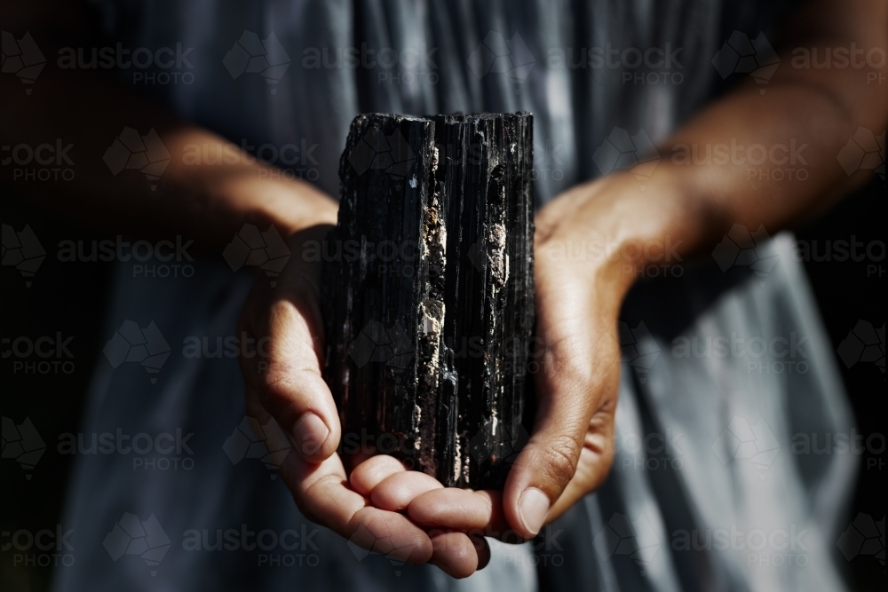 Woman's hands holding dark, black tourmaline crystal in healing concept - Australian Stock Image