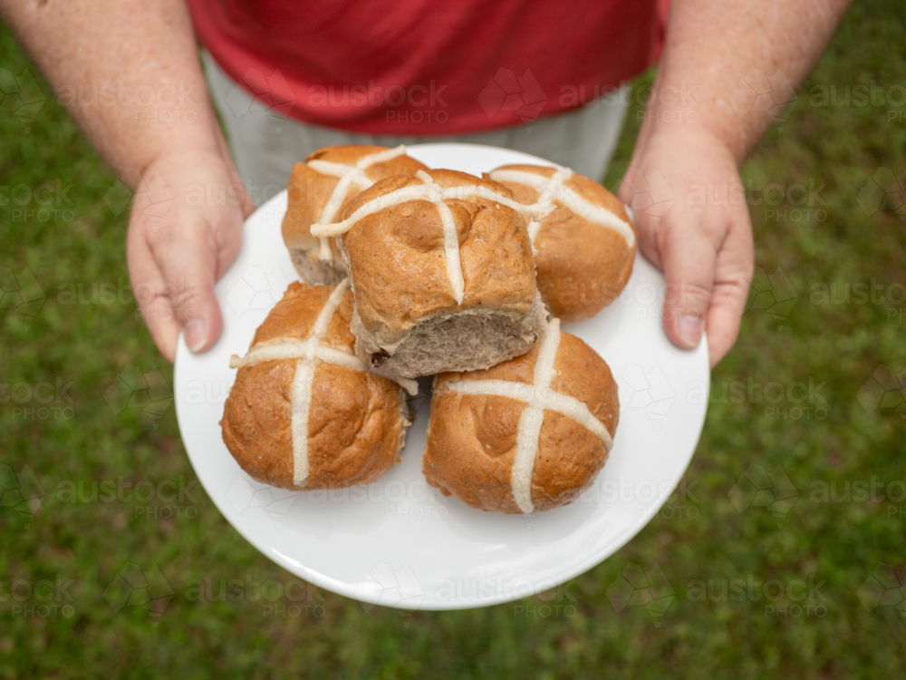 Woman's hands holding white plate of hot cross buns on green grass - Australian Stock Image