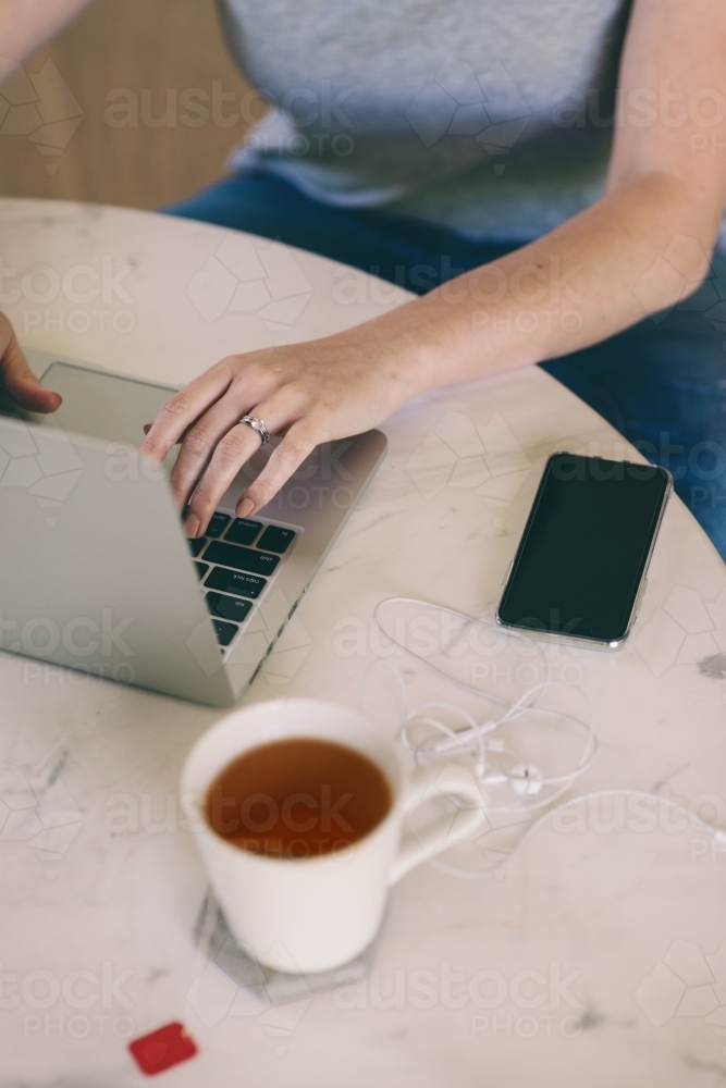 woman's working on laptop with tea and phone nearby - Australian Stock Image