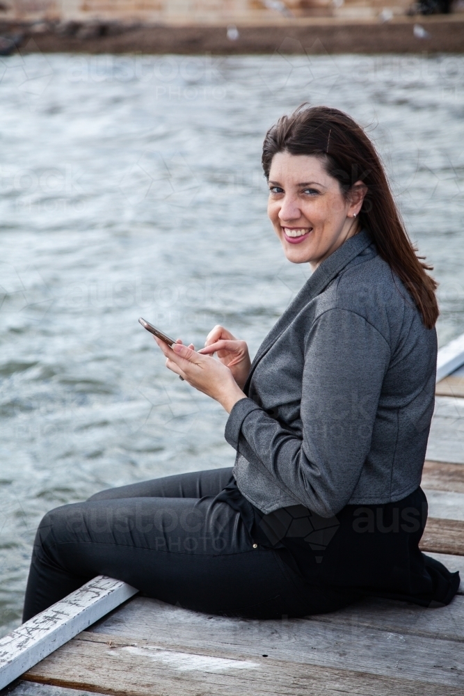 Woman seated on Warners Bay jetty with phone - Australian Stock Image