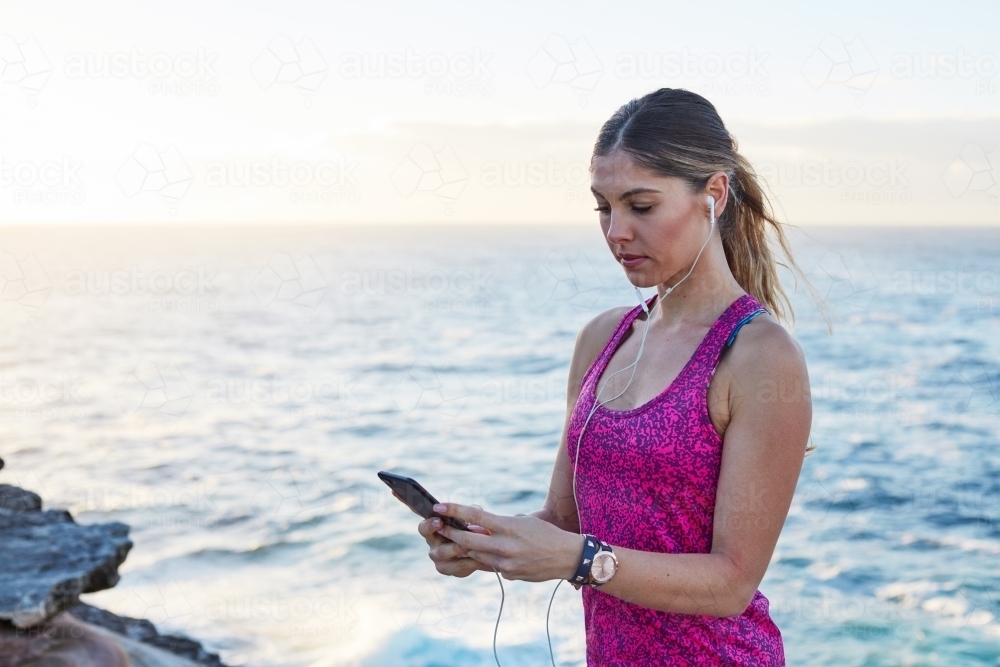 Woman selecting music track whilst exercising on coastline - Australian Stock Image