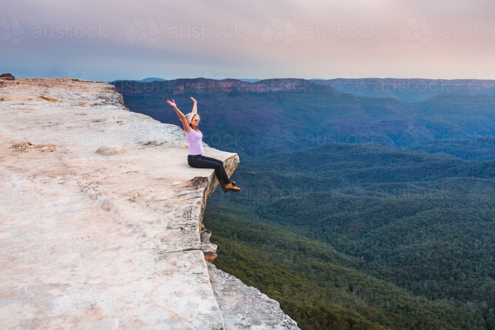 Woman showing emotional feelings of freedom and exhilaration sitting on the edge of the cliff - Australian Stock Image