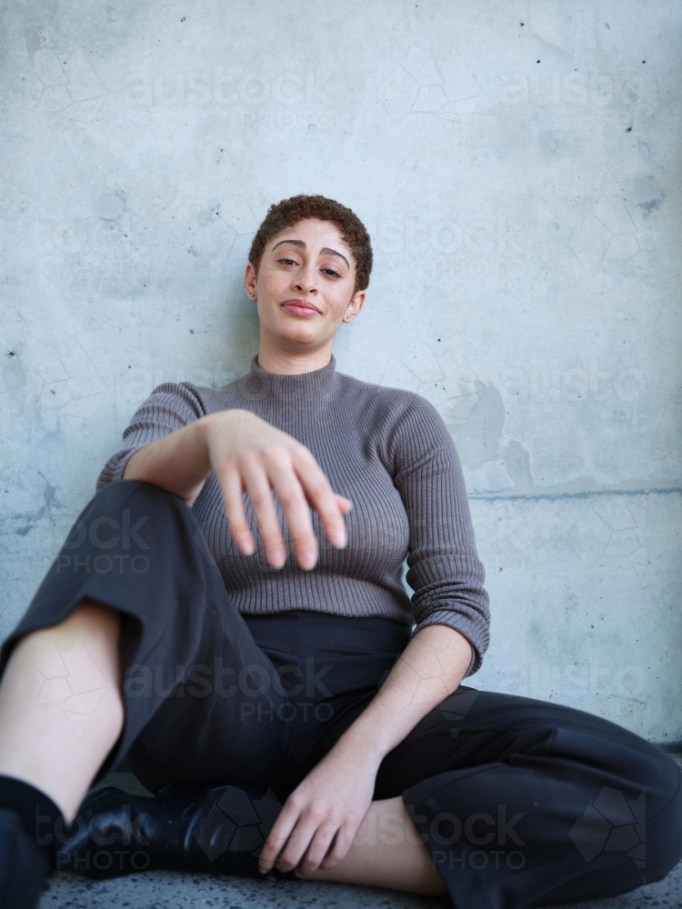 Image of Woman sitting against a concrete wall - Austockphoto