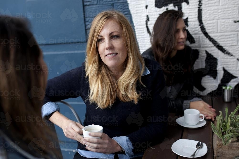 Woman sitting at a cafe listening to a friend - Australian Stock Image