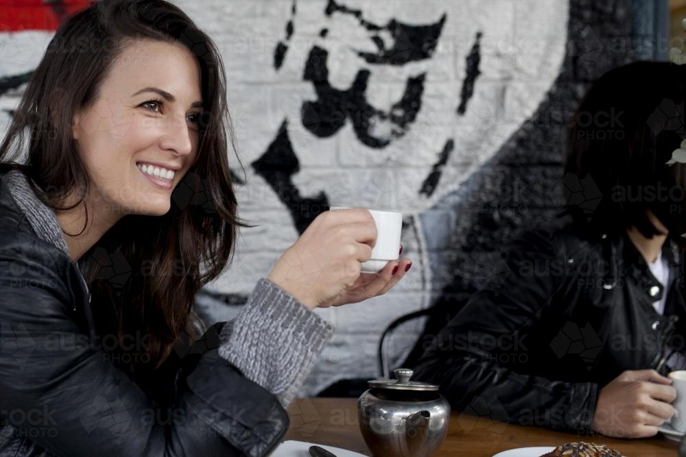 Woman sitting at cafe drinking tea and smiling - Australian Stock Image