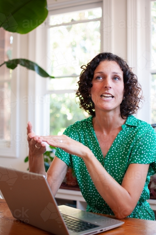 Woman sitting at laptop talking - Australian Stock Image
