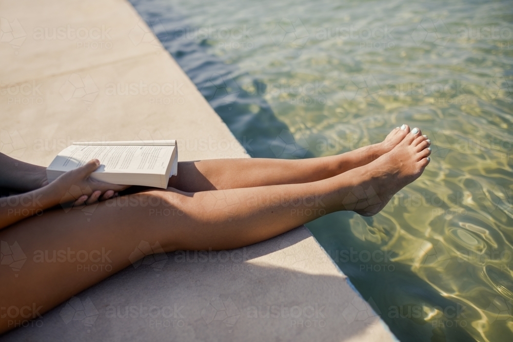 Woman sitting at pool's edge holding book - Australian Stock Image