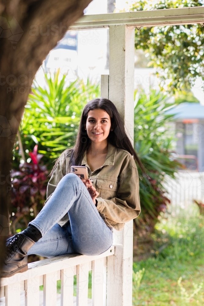 woman sitting fence, wearing jeans and black boots - Australian Stock Image