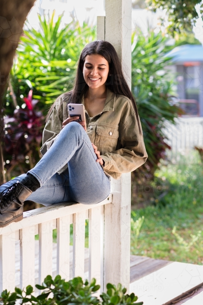 woman sitting fence, wearing jeans and black boots - Australian Stock Image