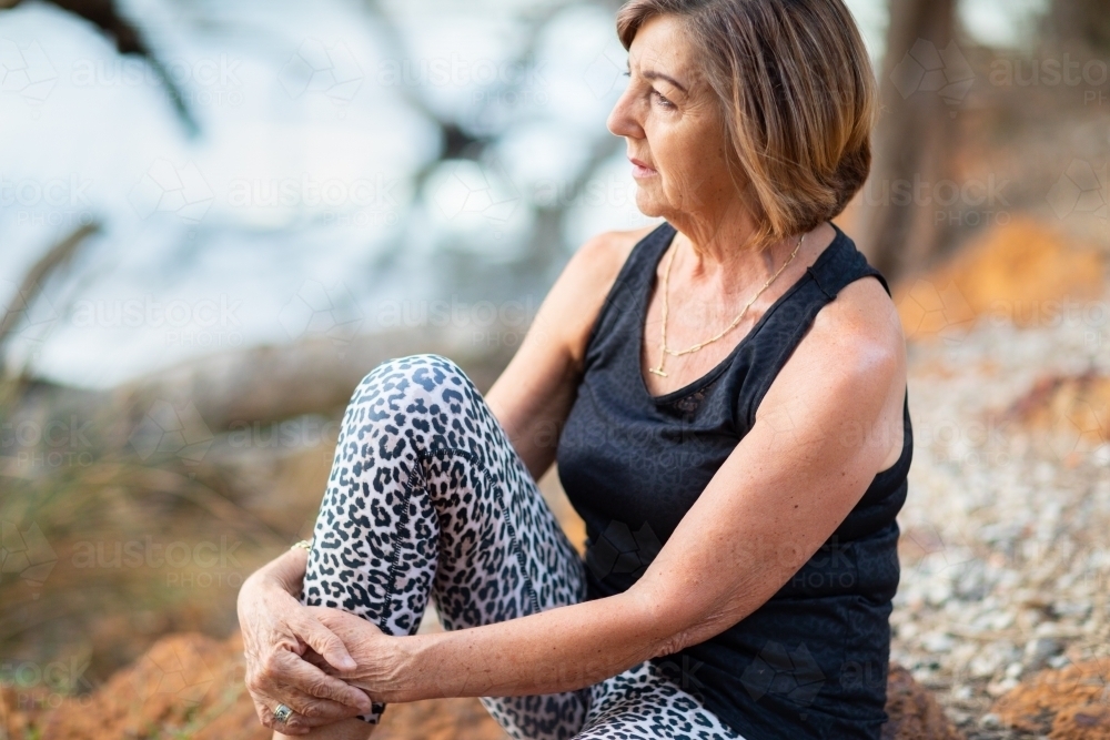 woman sitting in solitude with arms around knee - Australian Stock Image