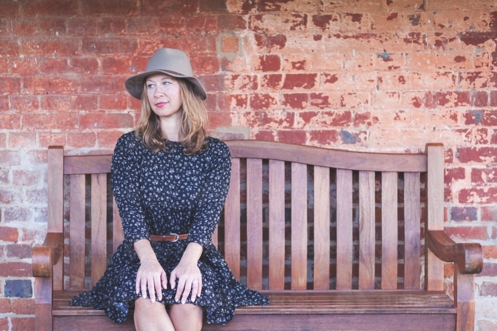 Woman sitting on a bench in front of a rustic wall - Australian Stock Image