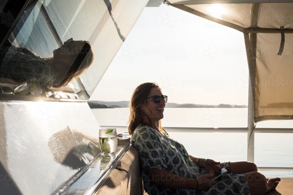 Woman sitting on cruiser boat enjoying drink at sunset - Australian Stock Image