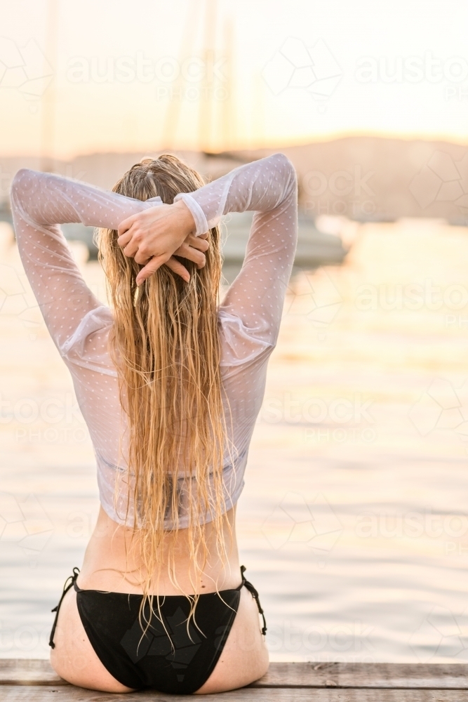 woman sitting on jetty looking at the ocean - Australian Stock Image