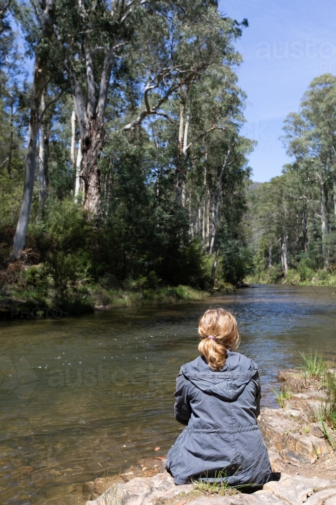Woman sitting on rocks by mountain stream - Australian Stock Image