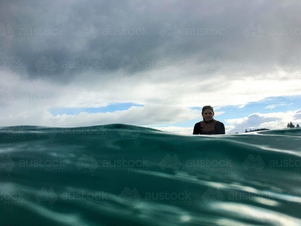 Woman sitting on surfboard in ocean with overcast sky backdrop - Australian Stock Image