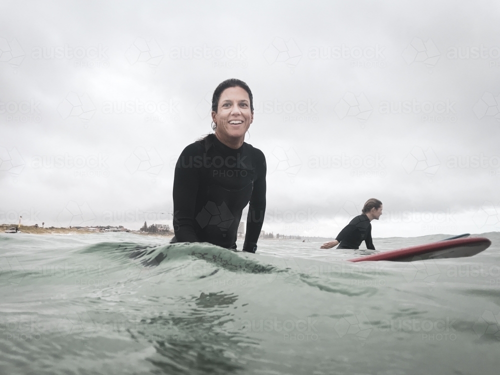 Woman sitting on surfboard looking at camera smiling - Australian Stock Image