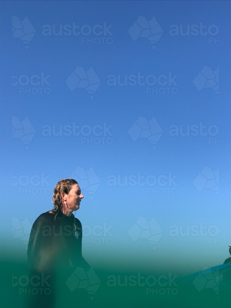 Woman sitting on surfboard submerged in water looking out to sea - Australian Stock Image