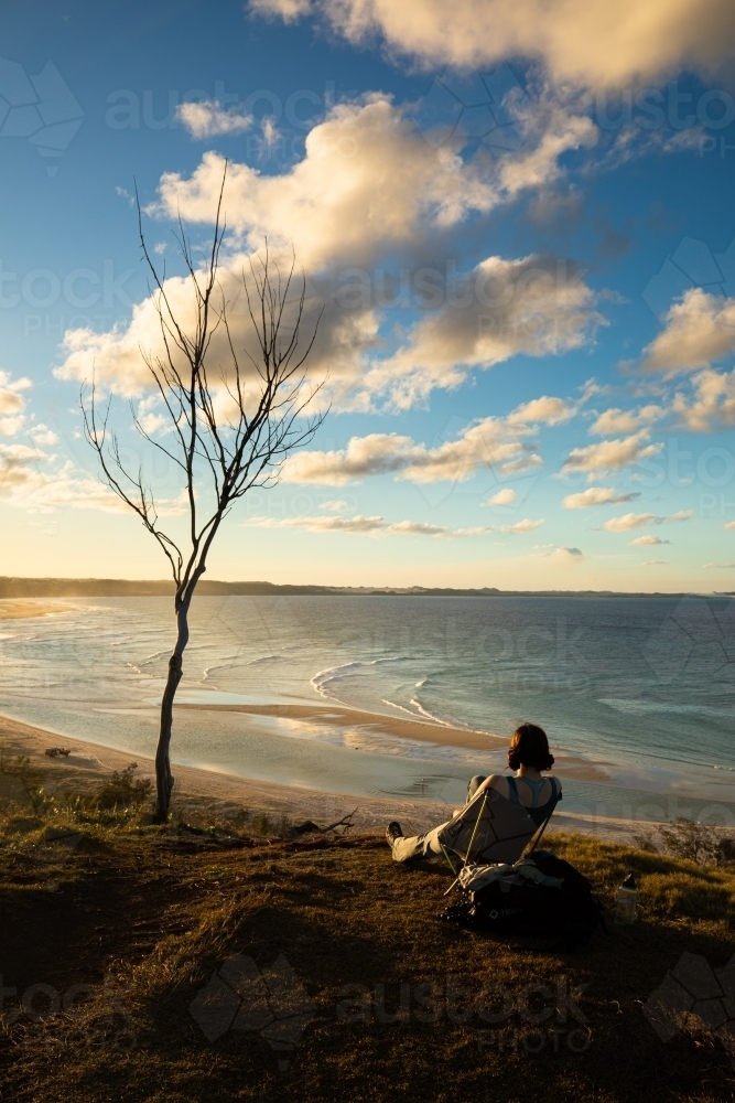 Woman sitting watching the sun set over Orchid Beach, Fraser Island - Australian Stock Image