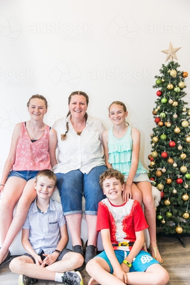 Woman sitting with four children with Christmas tree smiling - Australian Stock Image