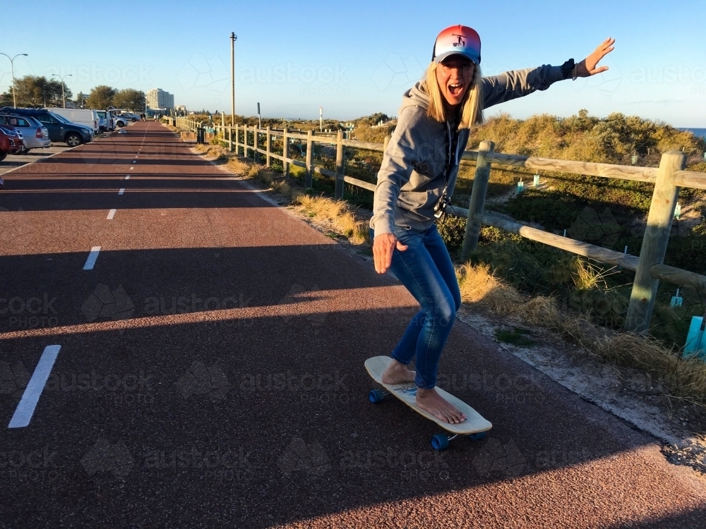 Woman skateboarding along coastal stretch in morning light - Australian Stock Image