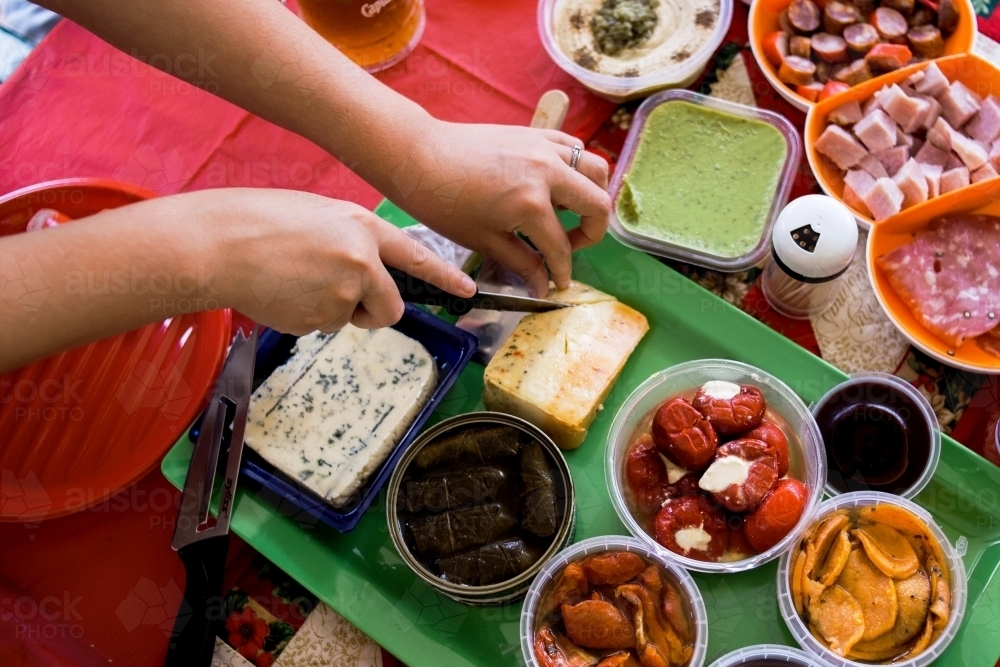 Woman slices multi coloured cheese from an antipasto platter at a Christmas party. - Australian Stock Image
