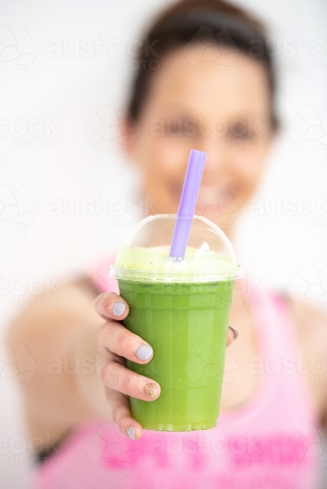 woman smiling holding green juice in workout clothes - Australian Stock Image