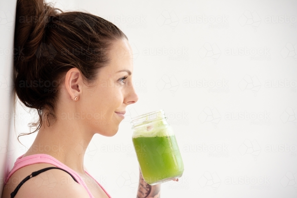 woman smiling holding healthy green juice on white background - Australian Stock Image