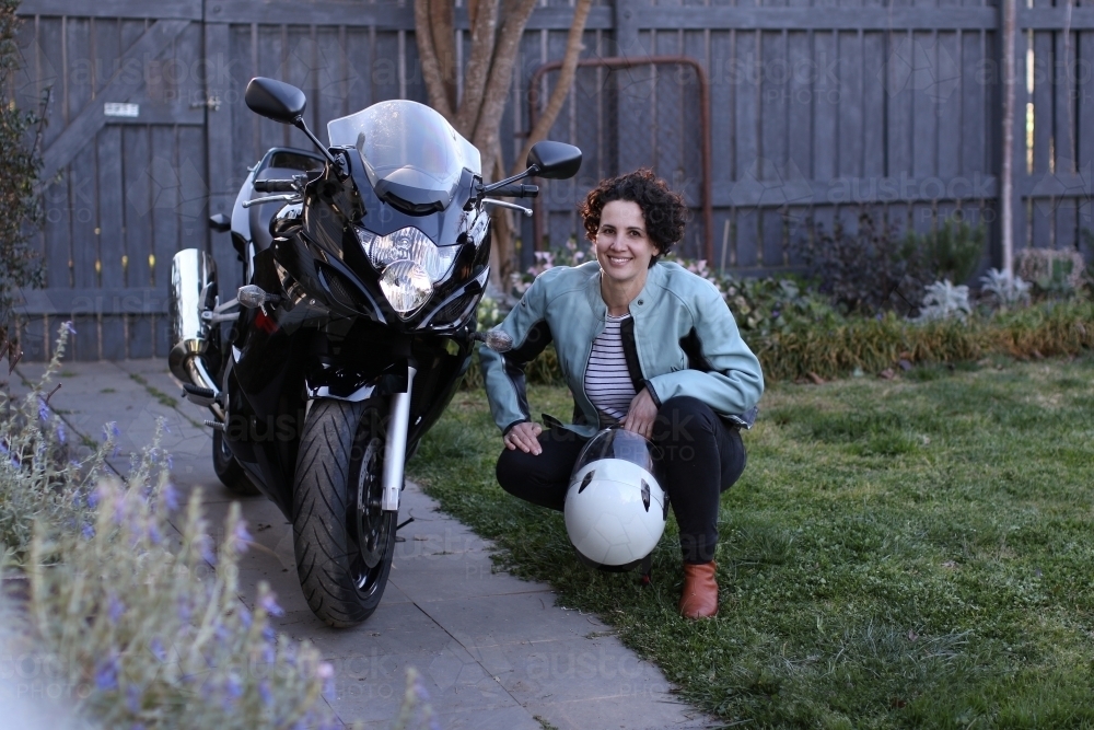 Woman smiling next to motorbike in garden - Australian Stock Image