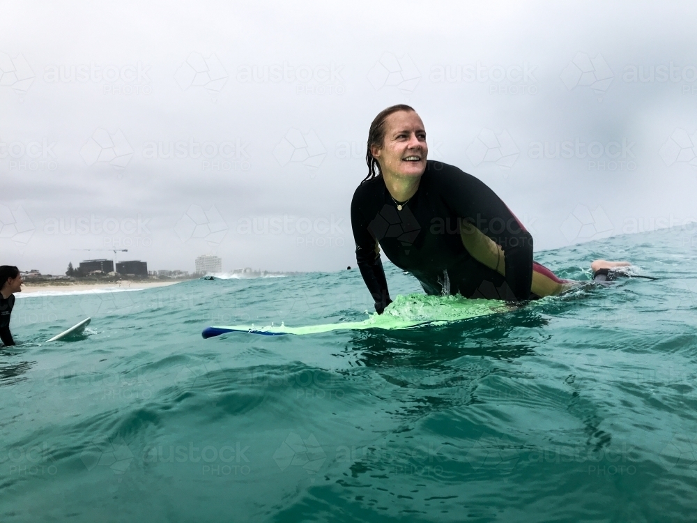 Woman smiling on surfboard in ocean on an overcast day - Australian Stock Image