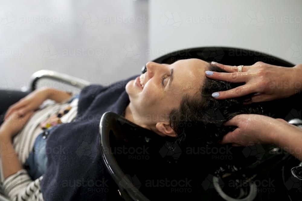 Woman smiling while having hair washed at hairdressing salon - Australian Stock Image