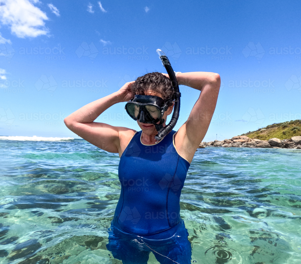 Woman snorkelling in clear blue green water adjusting snorkel and mask with sun shining - Australian Stock Image