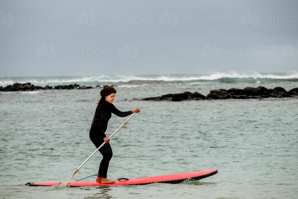 Woman stand up paddle boarding on the ocean. - Australian Stock Image