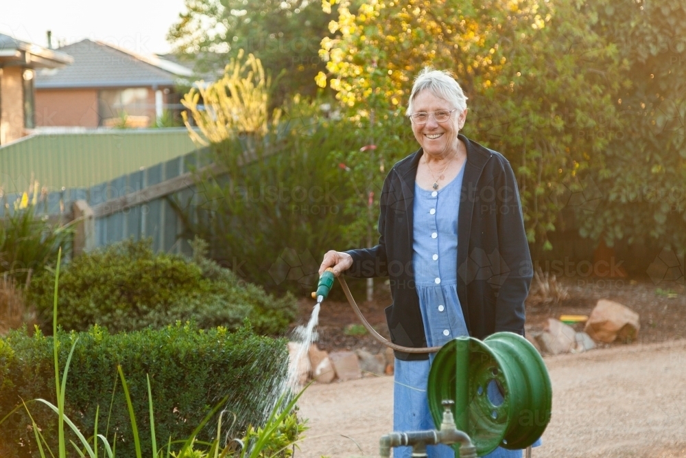 Woman standing at tap, watering front yard garden - Australian Stock Image