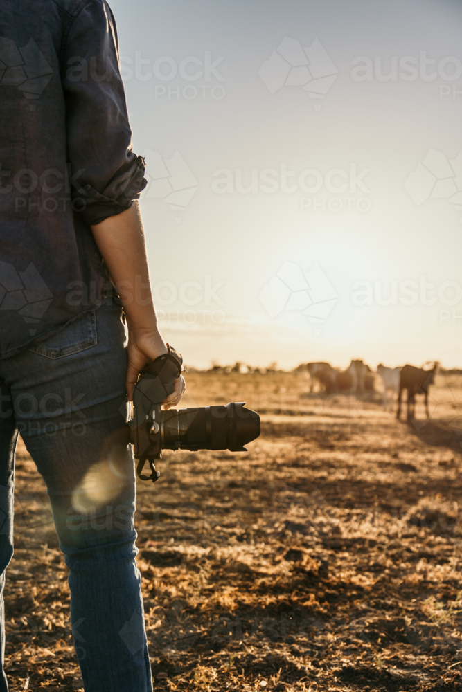 Woman standing in a dusty and dry grassy field holding a camera - Australian Stock Image