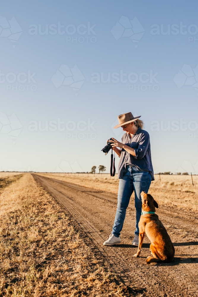 Woman standing in a dusty and dry grassy field holding a camera - Australian Stock Image