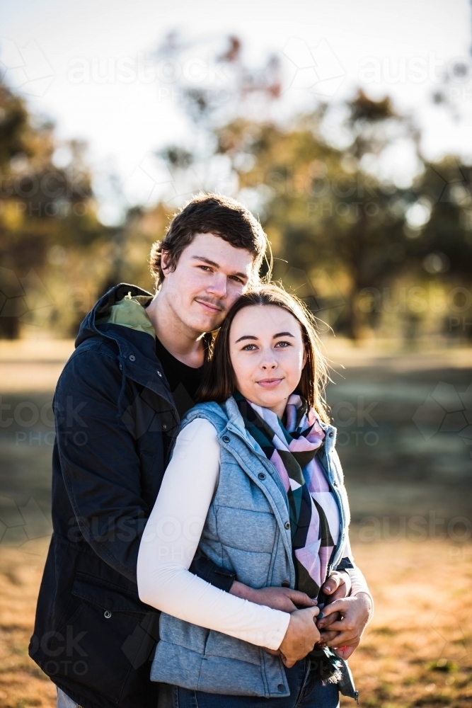 Woman standing in front of man his arms wrapped around her close together - Australian Stock Image