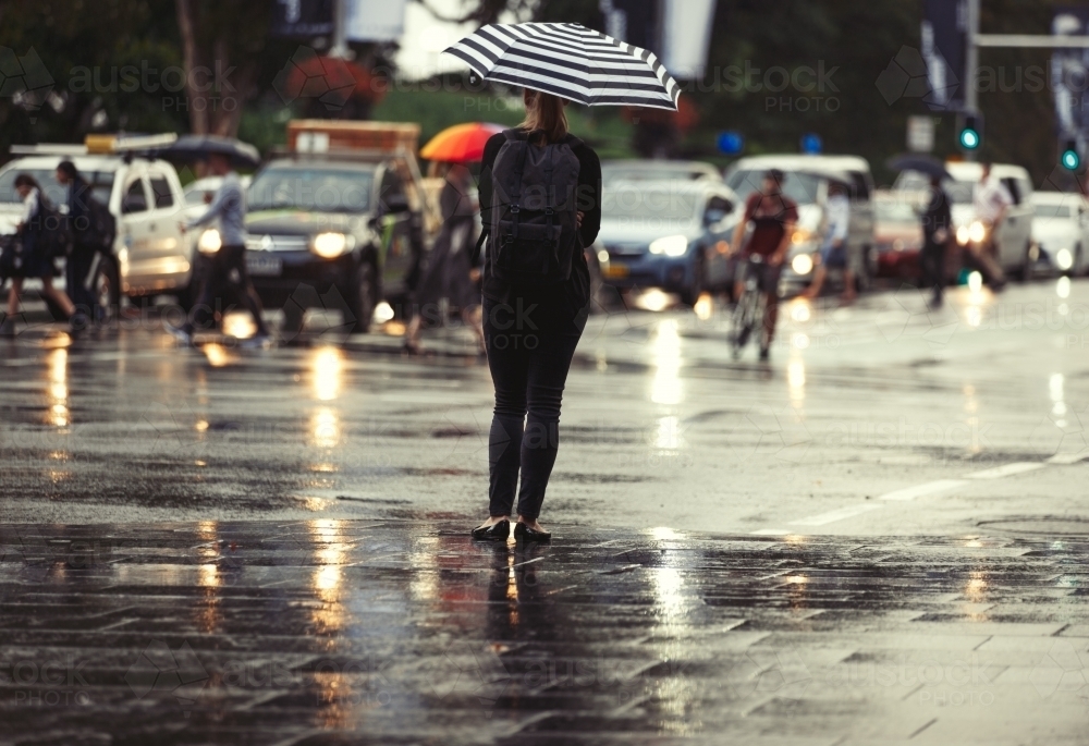 Woman standing in rain with striped umbrella - Australian Stock Image