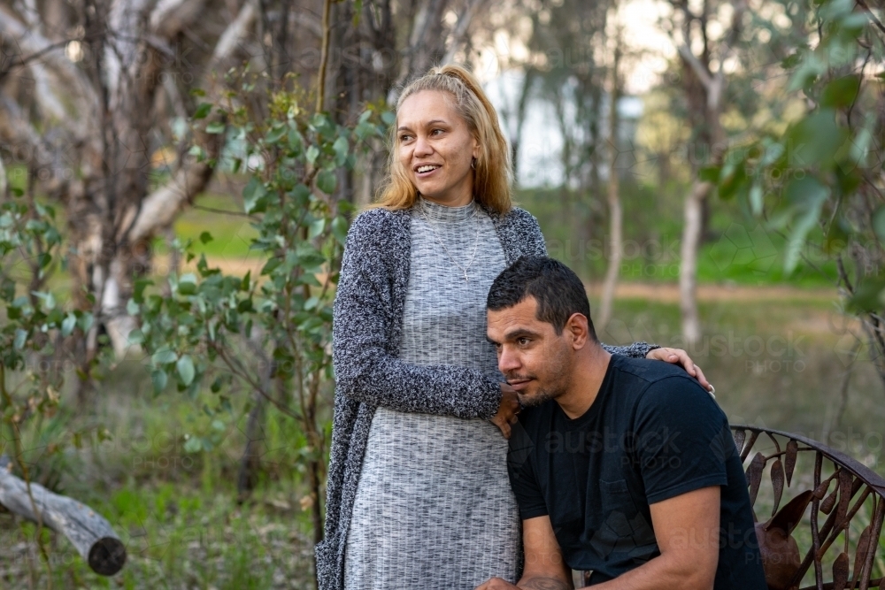 woman standing next to her man who is sitting on a park bench - Australian Stock Image