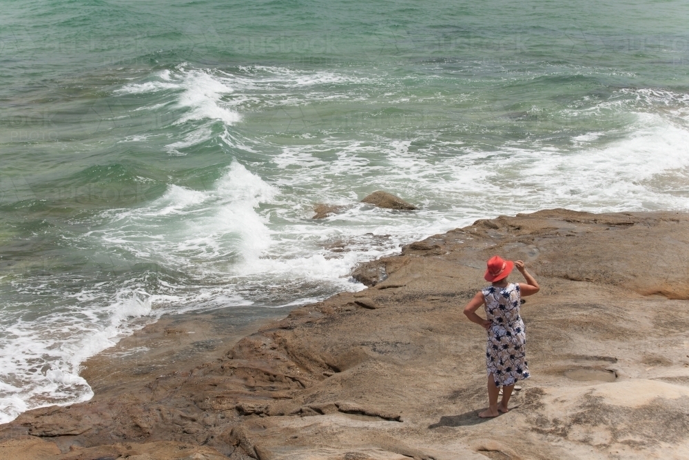 Woman standing on a rock looking out to the ocean - Australian Stock Image