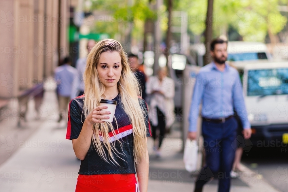 woman standing on busy city street with coffee - Australian Stock Image