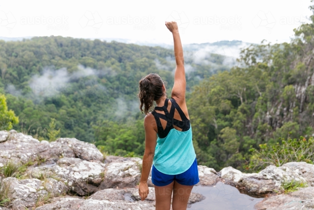 Woman standing on cliffs edge celebrating achievement above rainforest view below - Australian Stock Image