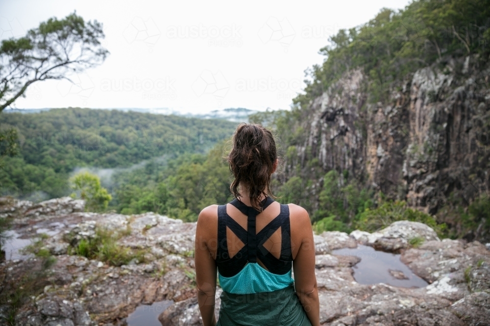 Woman Standing On Cliffs Edge Looking Out At The Rainforest View Below Woman Standing On Cliffs Edge Looking Out At The Rainforest View Below