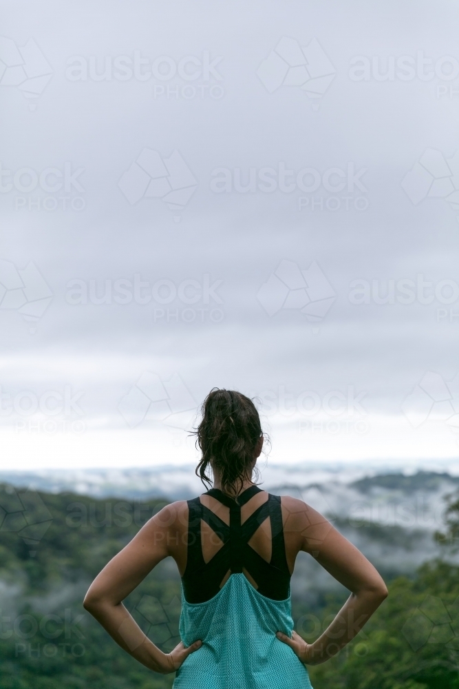Woman standing on cliffs edge looking out at the rainforest view below - Australian Stock Image